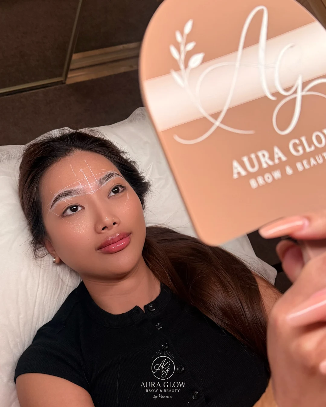 A client holding an Aura Glow mirror during brow mapping at the studio; an appointment photograph, not a before-and-after comparison.
